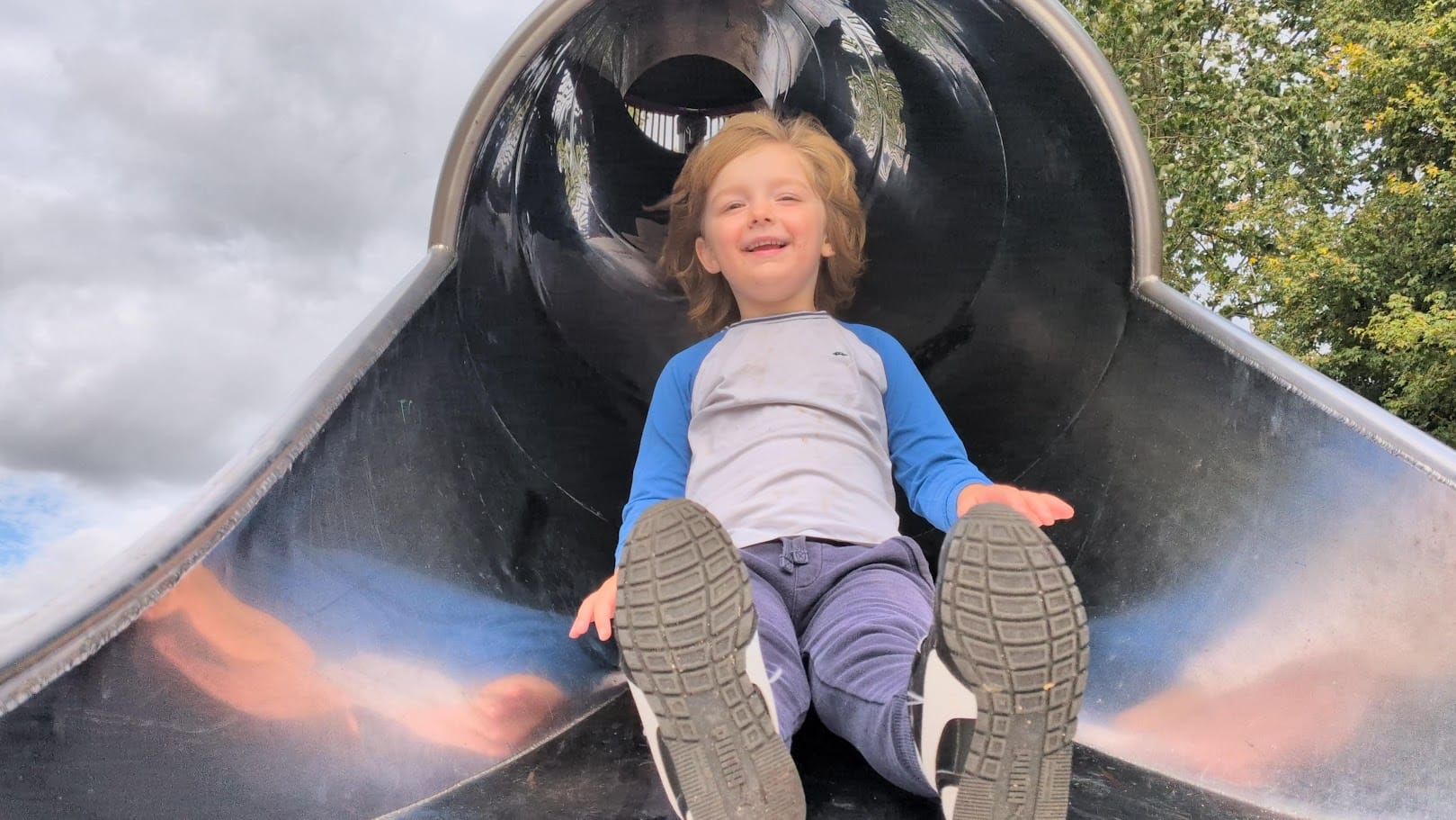 Oliver smiling while sliding down a park tunnel slide.