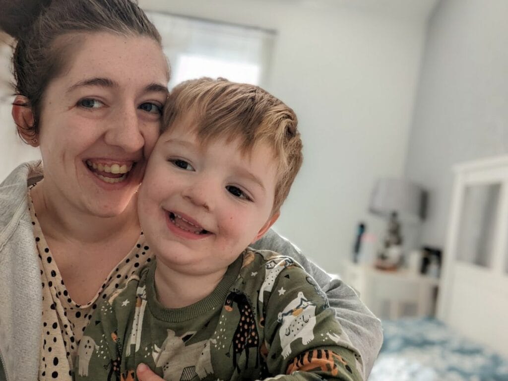 Oliver smiling while sitting with his mum at home.