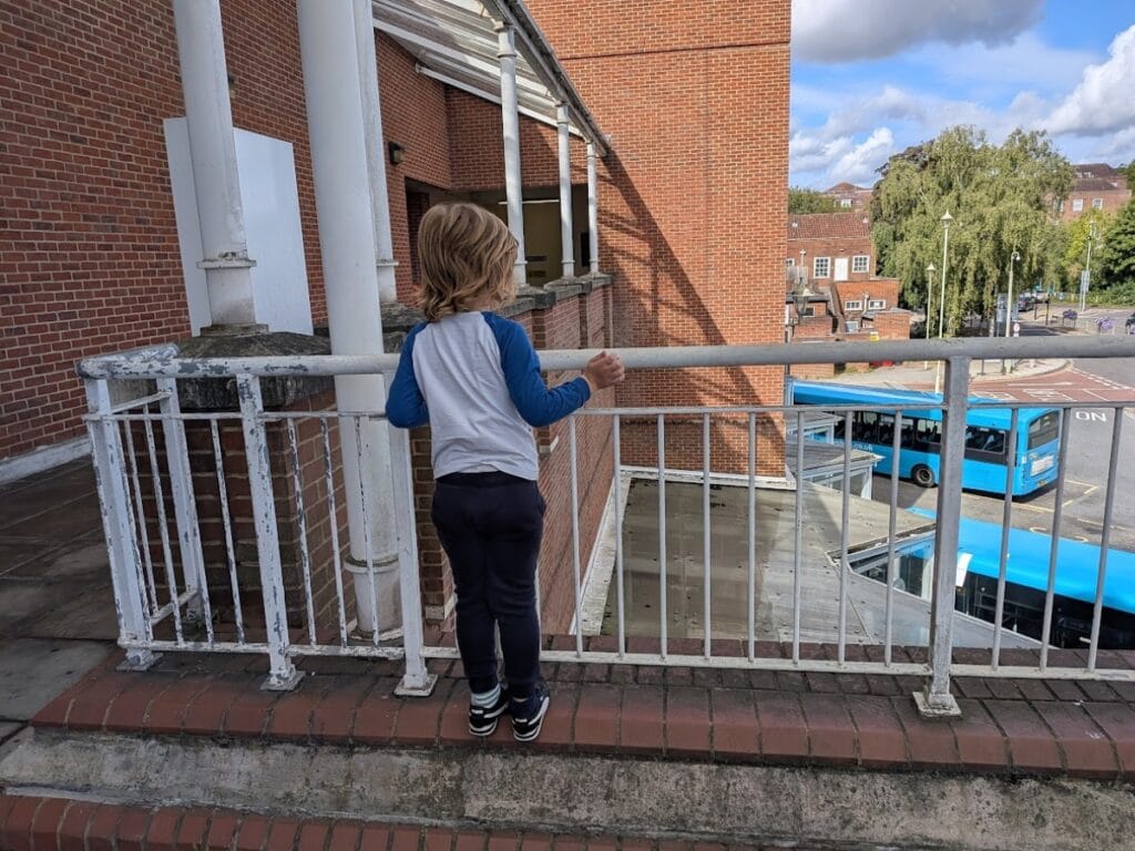 Oliver standing by a railing and looking down toward buses below.